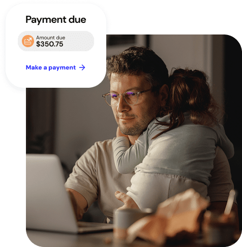 A father holds his daughter while using a laptop to make a payment while a graphic shows his payment due screen.