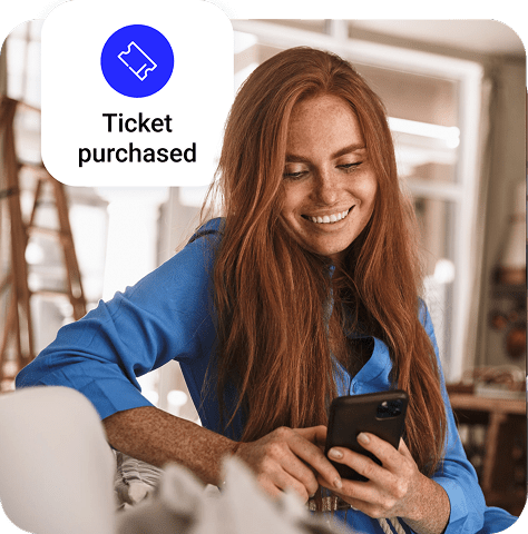 A merchant smiles while using their phone in their hand and is framed next to a small graphic that says “Ticket purchased.”
