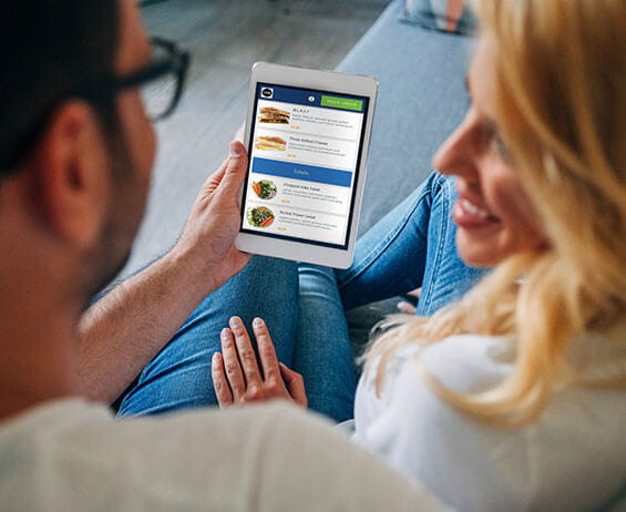 Young couple sitting on couch using online ordering app on mobile phone