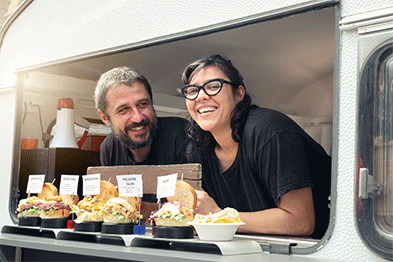 Two food vendors leaning out the window of a food truck